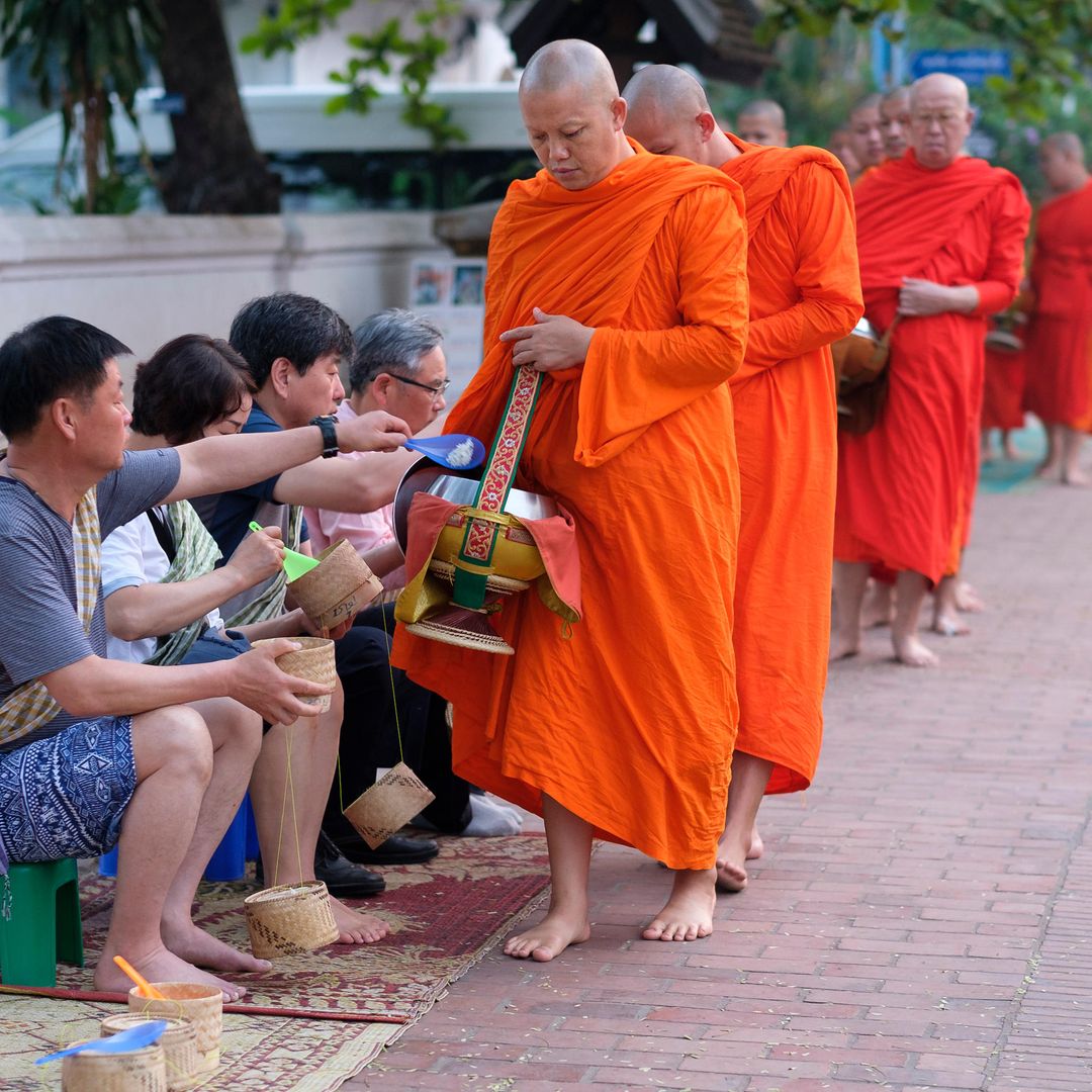 Procesión de monjes budistas vestidos con túnicas naranjas al amanecer para recoger regalos en las calles de Luang Prabang, Laos, Asia