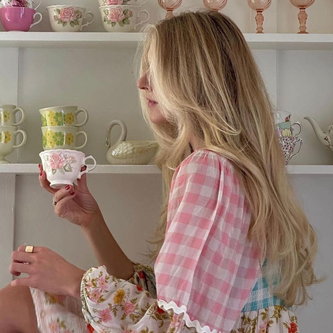 Chica con pelo rubio y vestido romántico de cuadros sujetando una taza de té