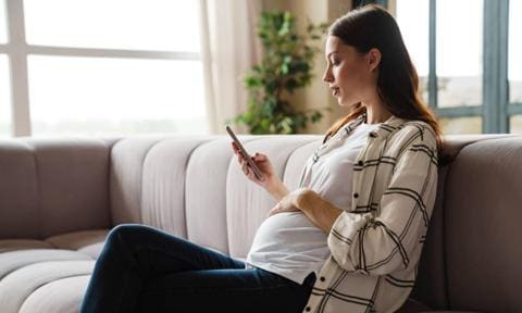 Mujer embarazada con móvil en la mano sentada en un sofá