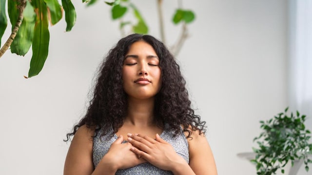 A beautiful and young multiracial woman is doing breathing exercise at home.