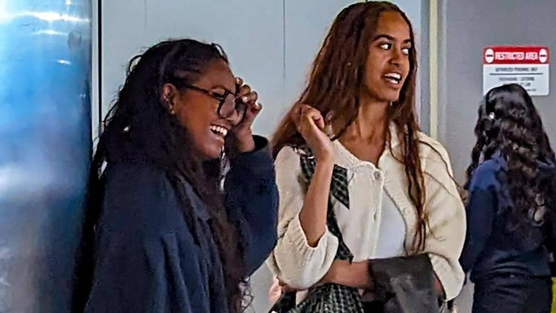 Malia and Sasha Obama laugh together as they wait to board their plane at LAX