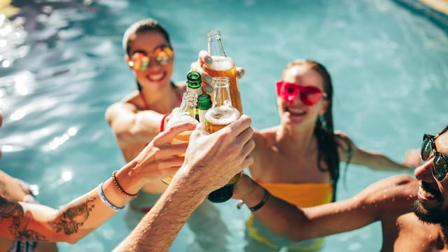 Happy group of young people in swimming pool drinking beers. Multiracial friends enjoying and toasting drinks during a pool party.