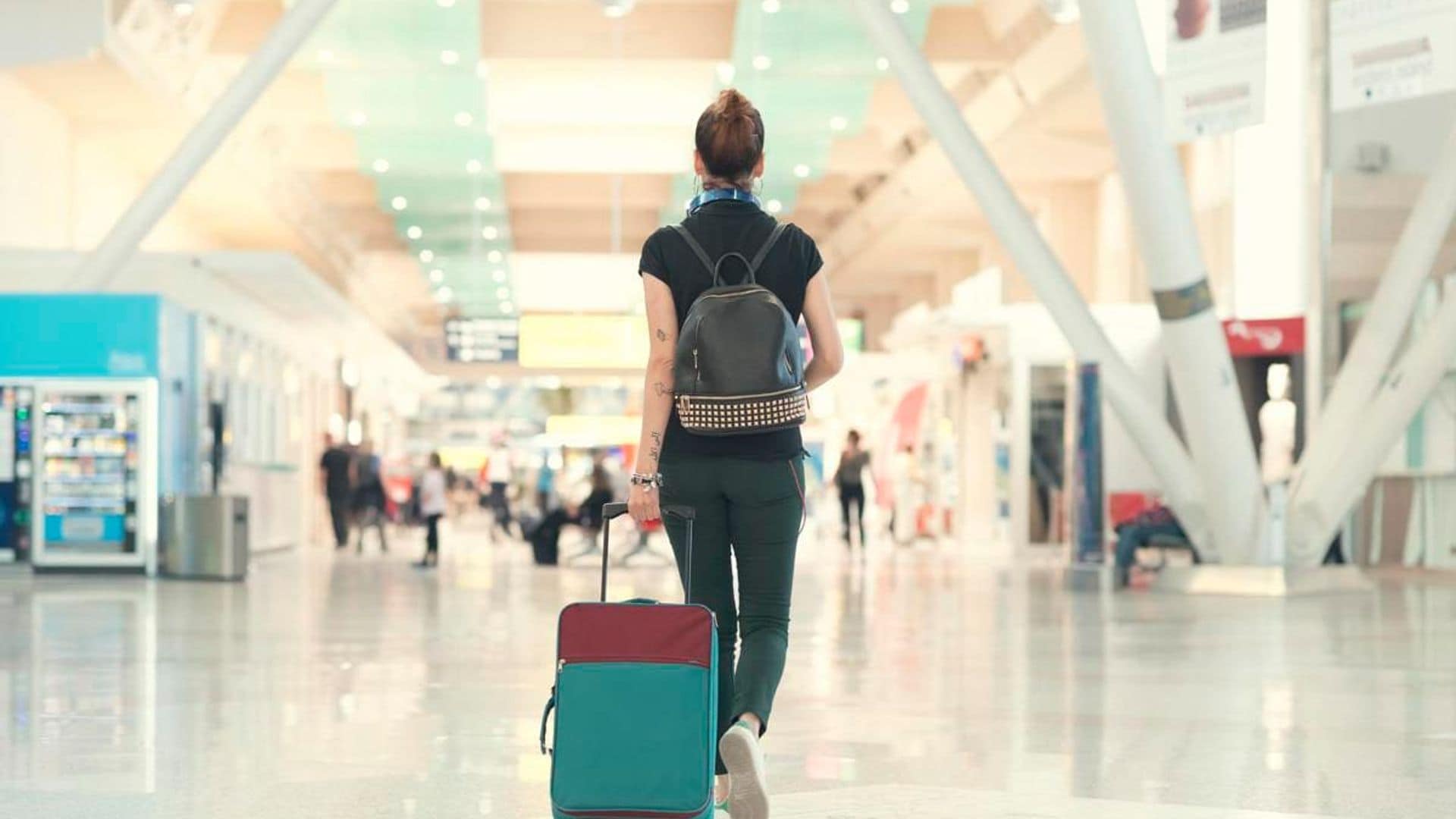 Back view of woman pulling her luggage strolling inside the airport terminal