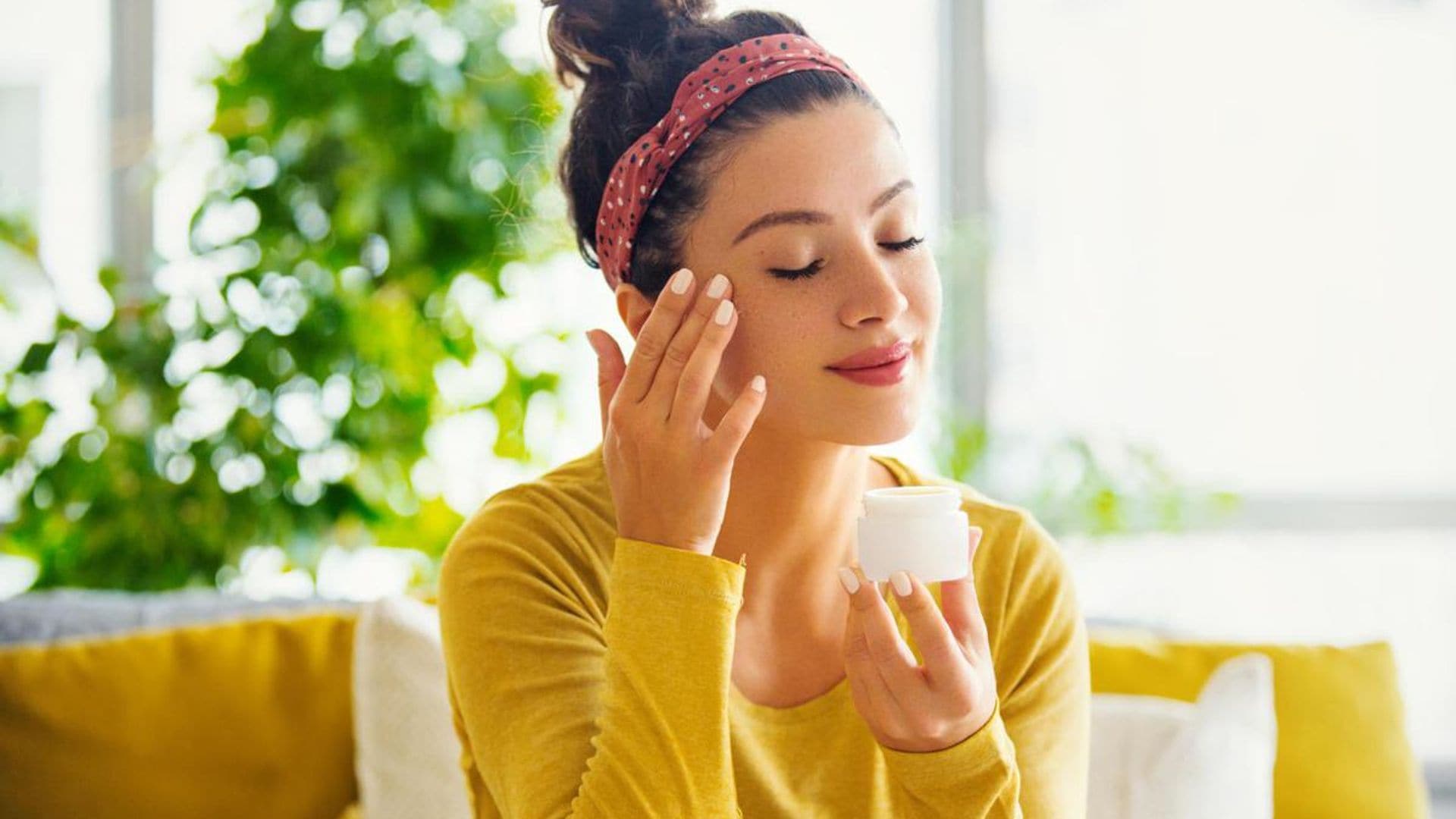 Young woman with eyes closed applying face cream.