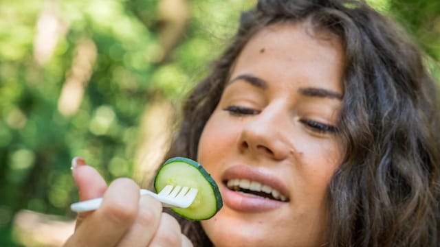 Girl seating on the bench in the woods and eating salad