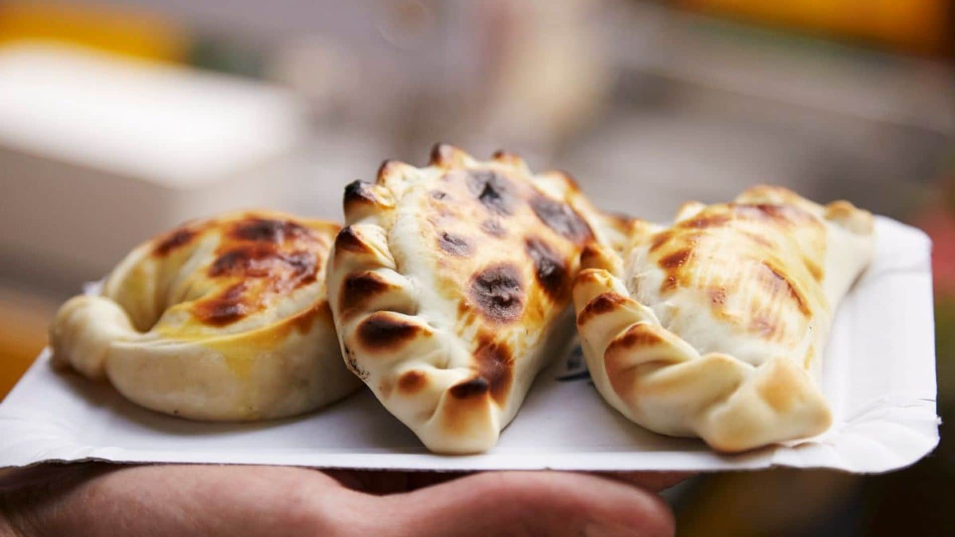 A hand holding a paper plate of empanadas at a market