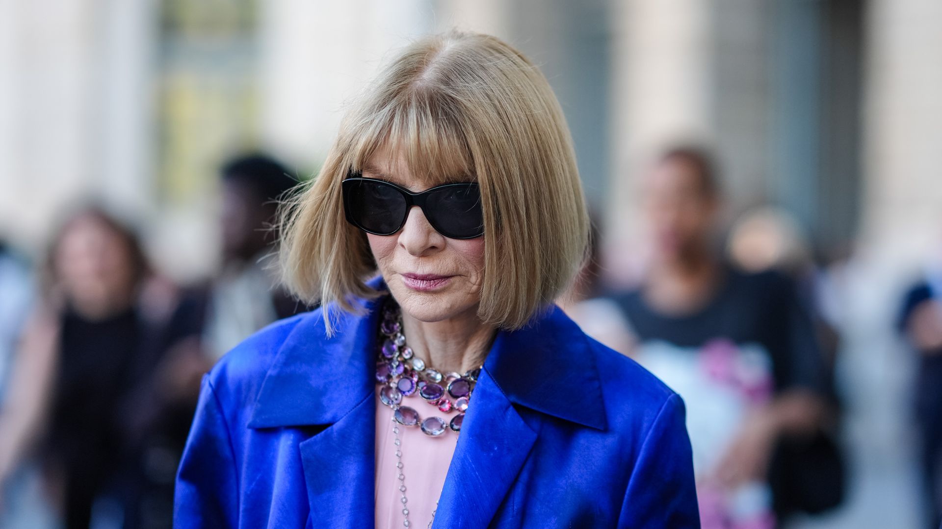 Anna Wintour wears black sunglasses, silver dark purple, and light pink layered clear gemstone necklaces, navy blue, pink, and brown brush stroke Dries Van Noten blazer coat outside Giambattista Valli during the Paris Haute Couture Week Fall/Winter 2024-2025 on June 24, 2024, in Paris, France. 