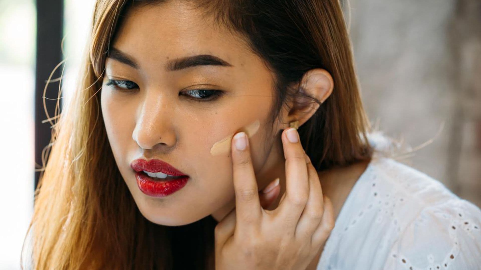 Closeup young Asian woman with red lips applying corrector on face on blurred background