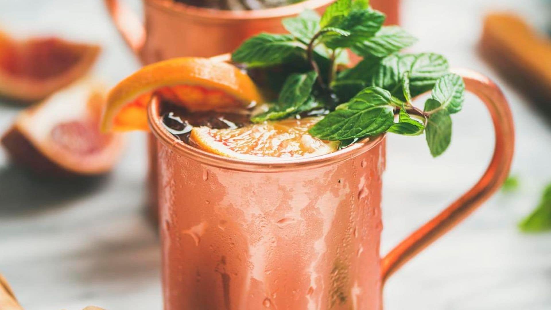 Blood orange Moscow mule alcohol cocktails with fresh mint leaves and ice in copper mugs over white marble background