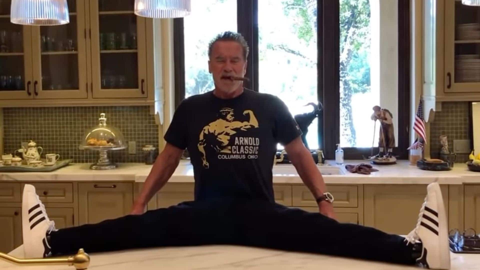 Arnold Schwarzenegger appears to do the splits on his kitchen counter while smoking a cigar