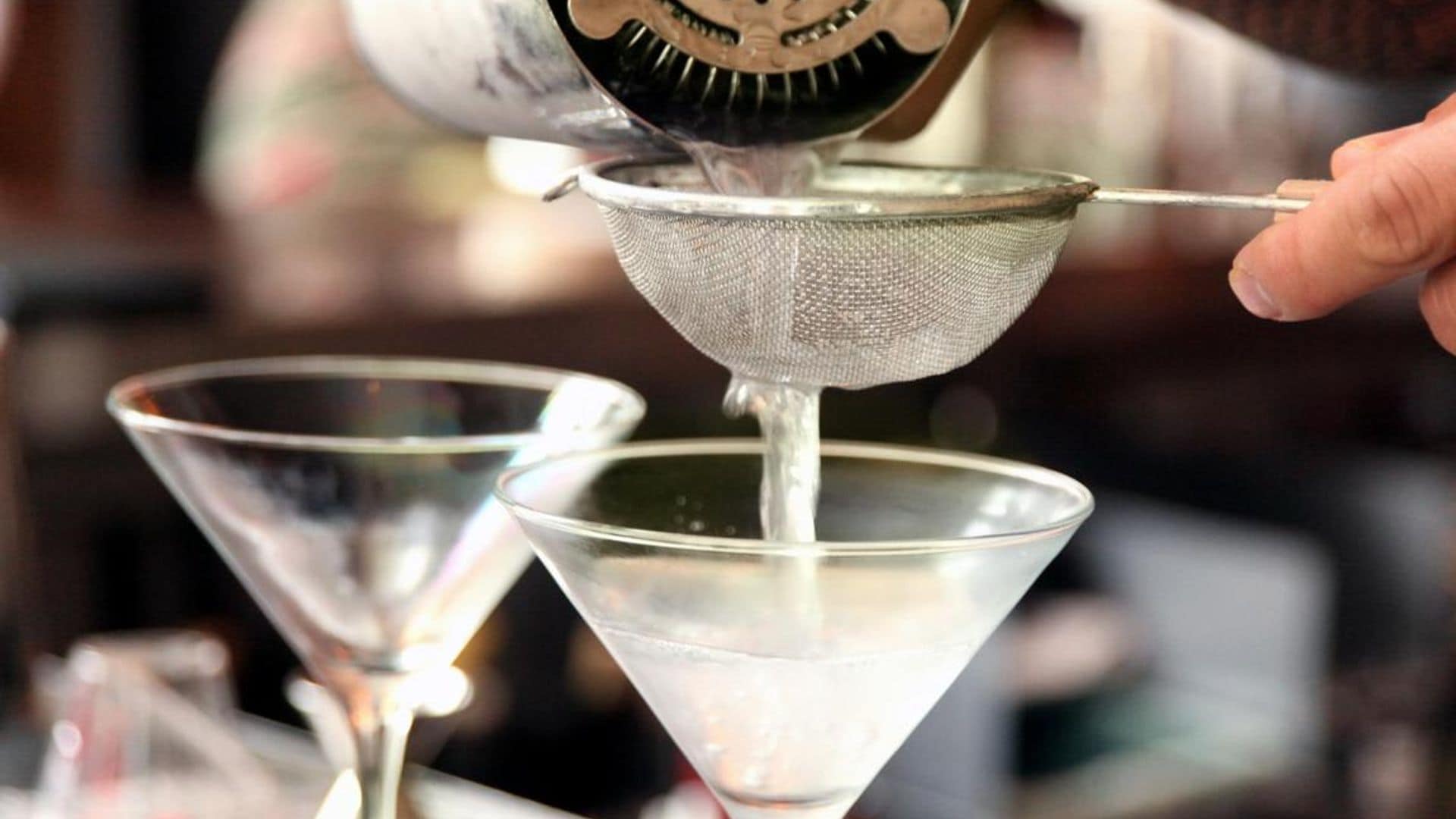 a bartender pouring martinis into chilled glasses through a small wire mesh strainer.