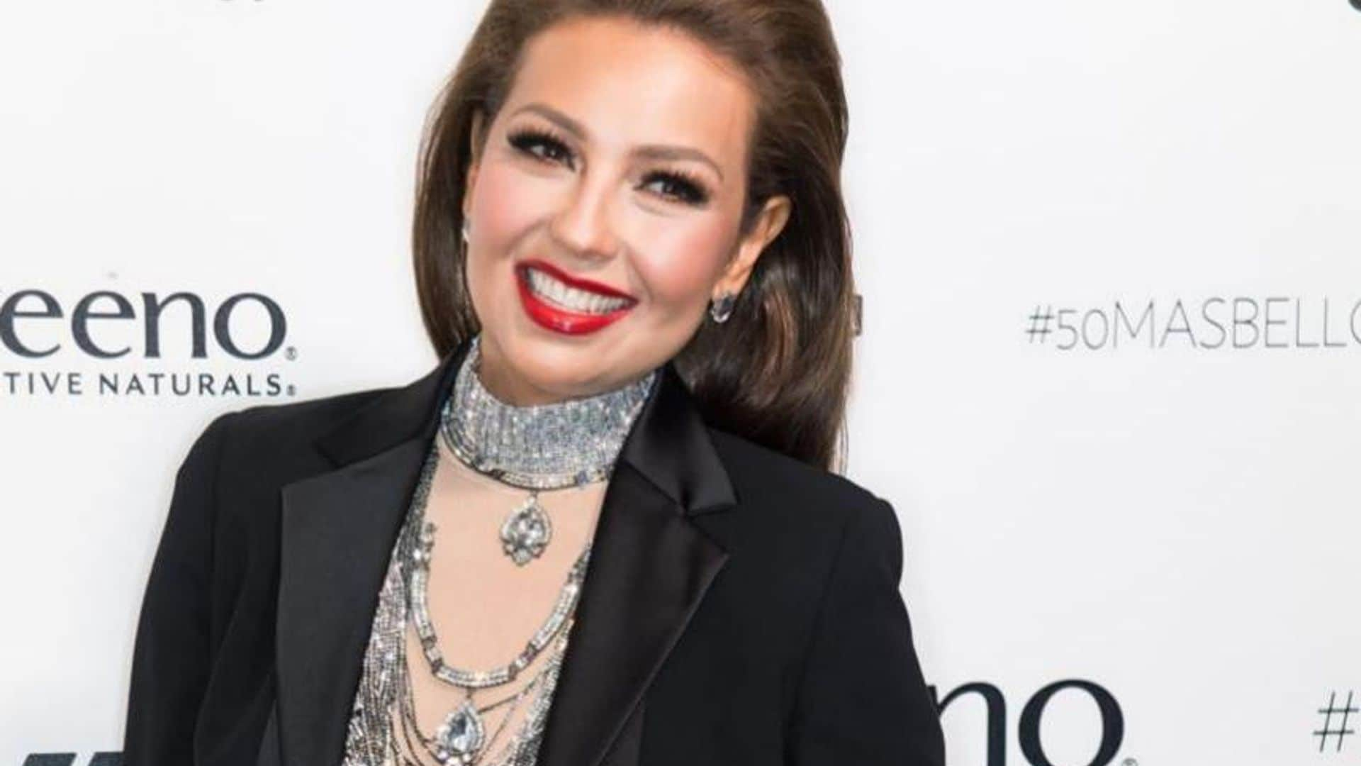 Thalia with her hair down, red lips, blouse with transparencies, and blazer.