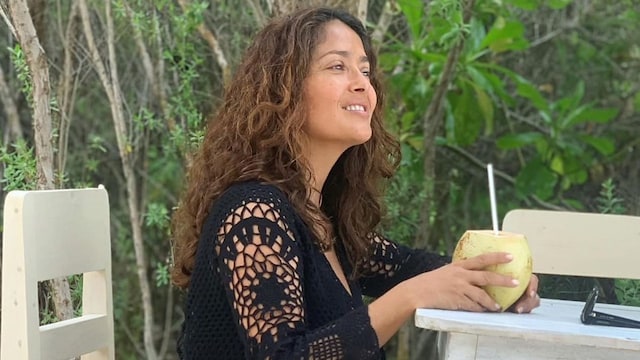 Salma Hayek wearing crochet dress and drinking coconut water.