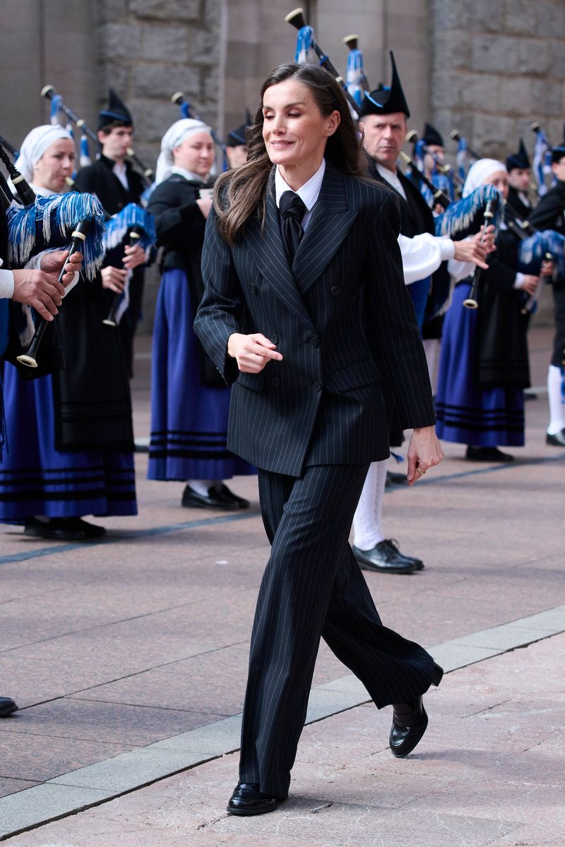 Make it more descriptive

Queen Letizia transforms her look in Oviedo, stepping out in a striking masculine pinstripe suit featuring sharp, diplomatic stripes, paired with a stylish scarf creatively knotted as a tie for an unexpected twist.

