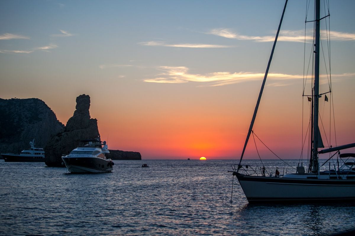 Two boats anchored with Illa des Bosc in the distance while sun is setting in the mediterranean horizon