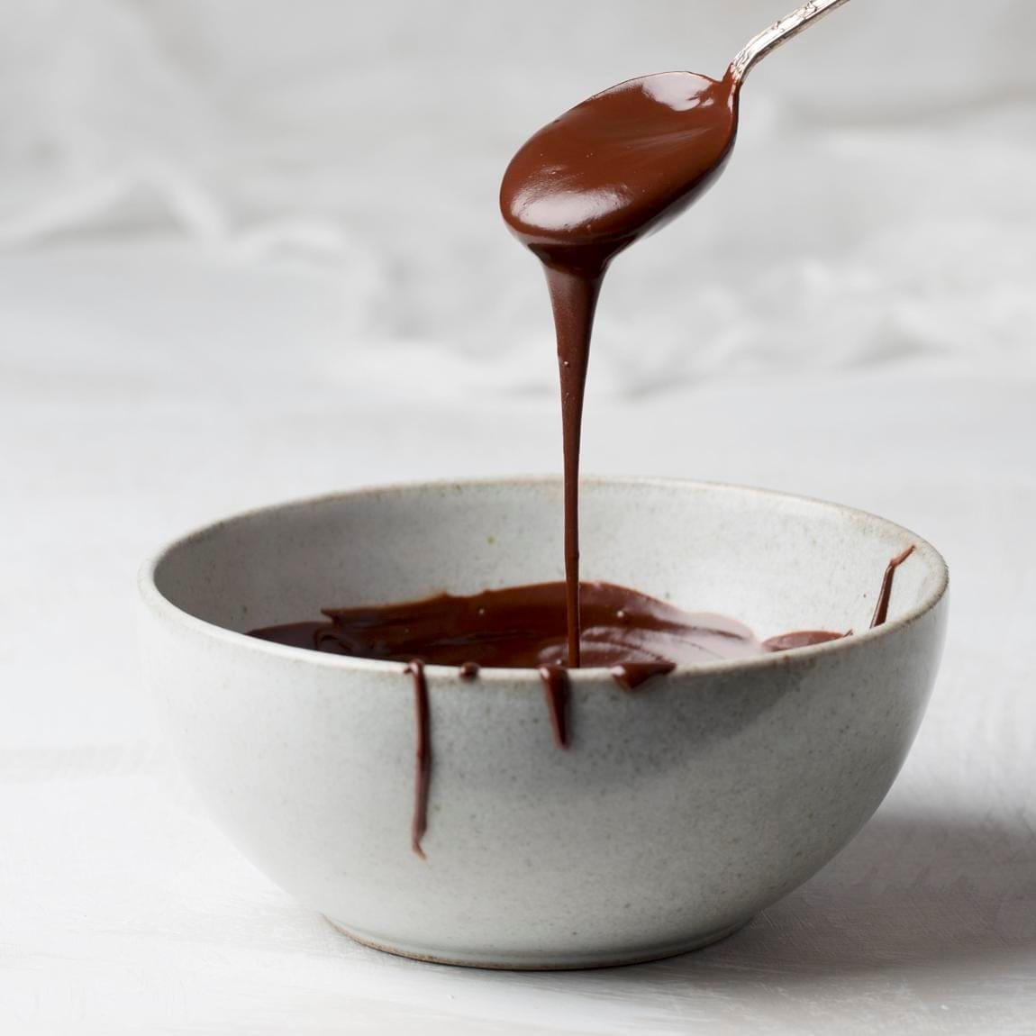 Melted dark organic chocolate dripping from a spoon into a bowl