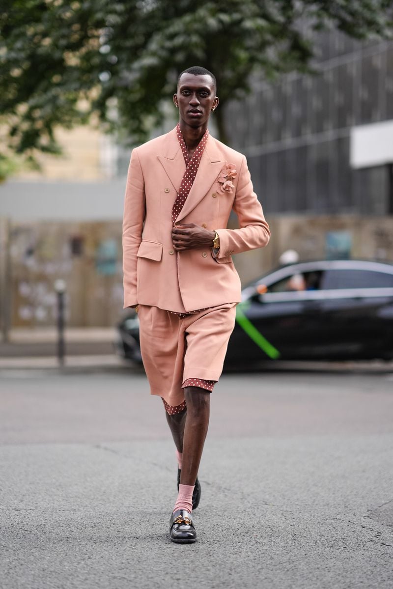 A person wears gold hoop earrings, a pink and white polka-dotted shirt, a beige pink double-breasted suit blazer jacket with floral detail, beige pink shorts lined with pink and white polka dots, pink socks, and shiny black loafer leather shoes outside Amiri on June 20, 2024, during the Paris Fashion Week Menswear Spring/Summer 2025 in Paris, France. 