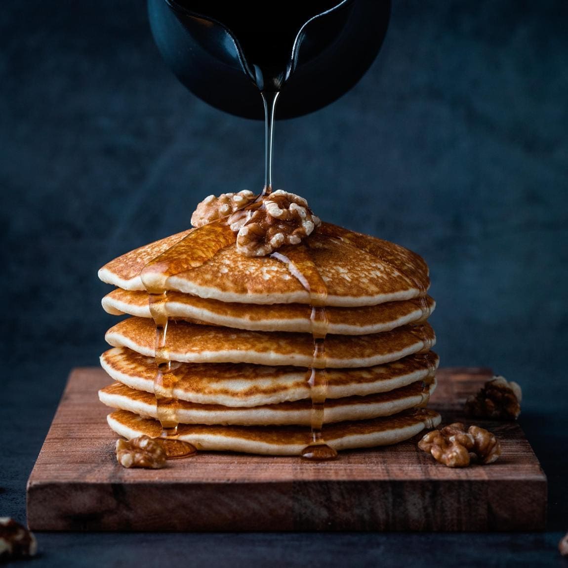 Stack of pancakes topped with walnuts and syrup being poured on top