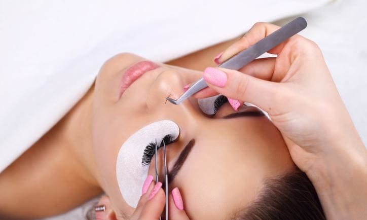 Young woman having eyelash extensions put on, lash by lash, with tweezers