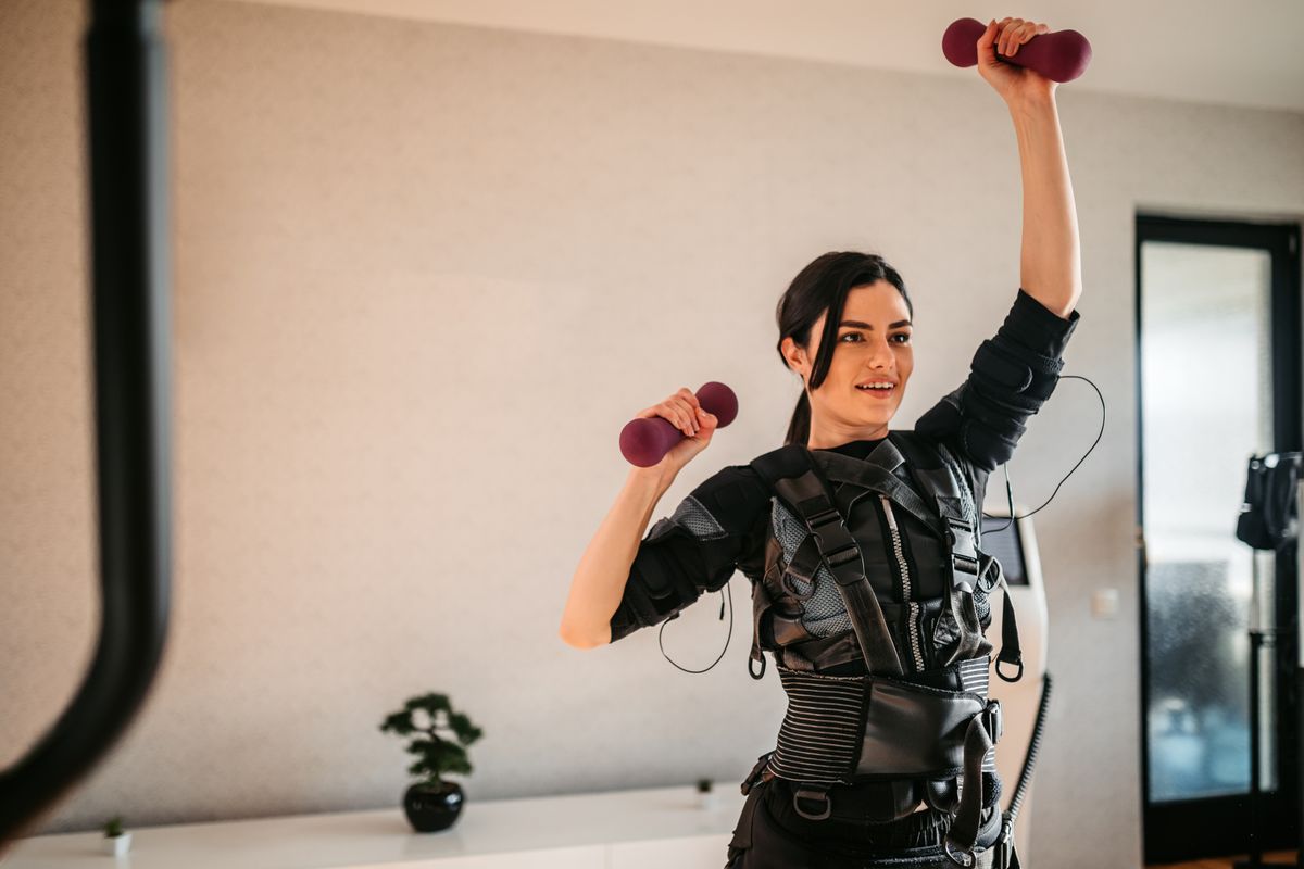 A woman wears an EMS suit while training with dumbbells