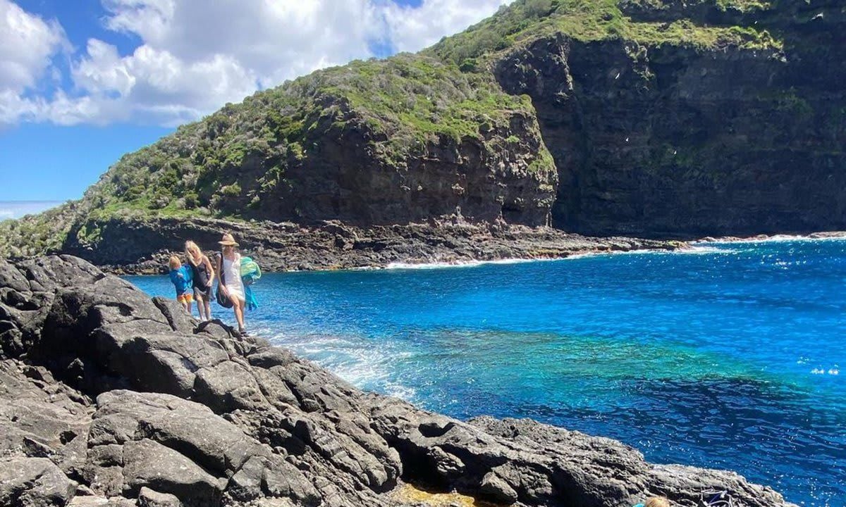 Una vista aérea del océano y las piscinas naturales. 4 personas caminan sobre un puente de roca.