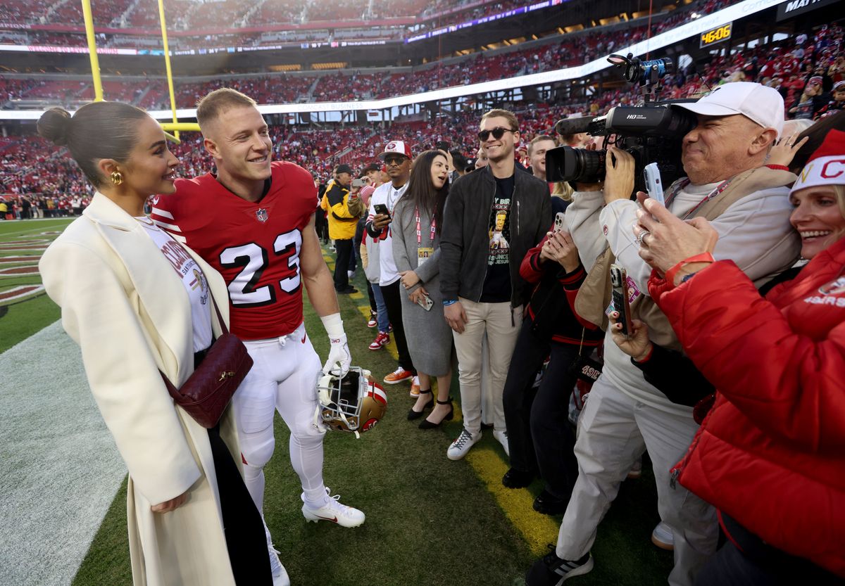 Olivia Culpo and Christian McCaffrey on the field as fans and media capture the moment before a 49ers game.