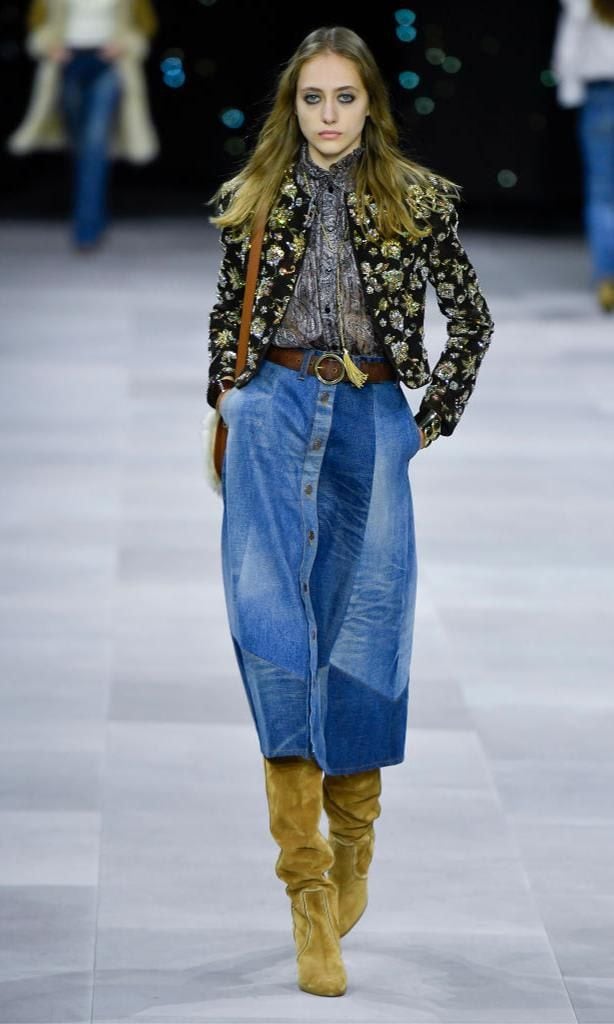 A model walks the catwalk at the Celine fashion show wearing an outfit combining a sweater, blouse, and denim skirt with the patchwork technique