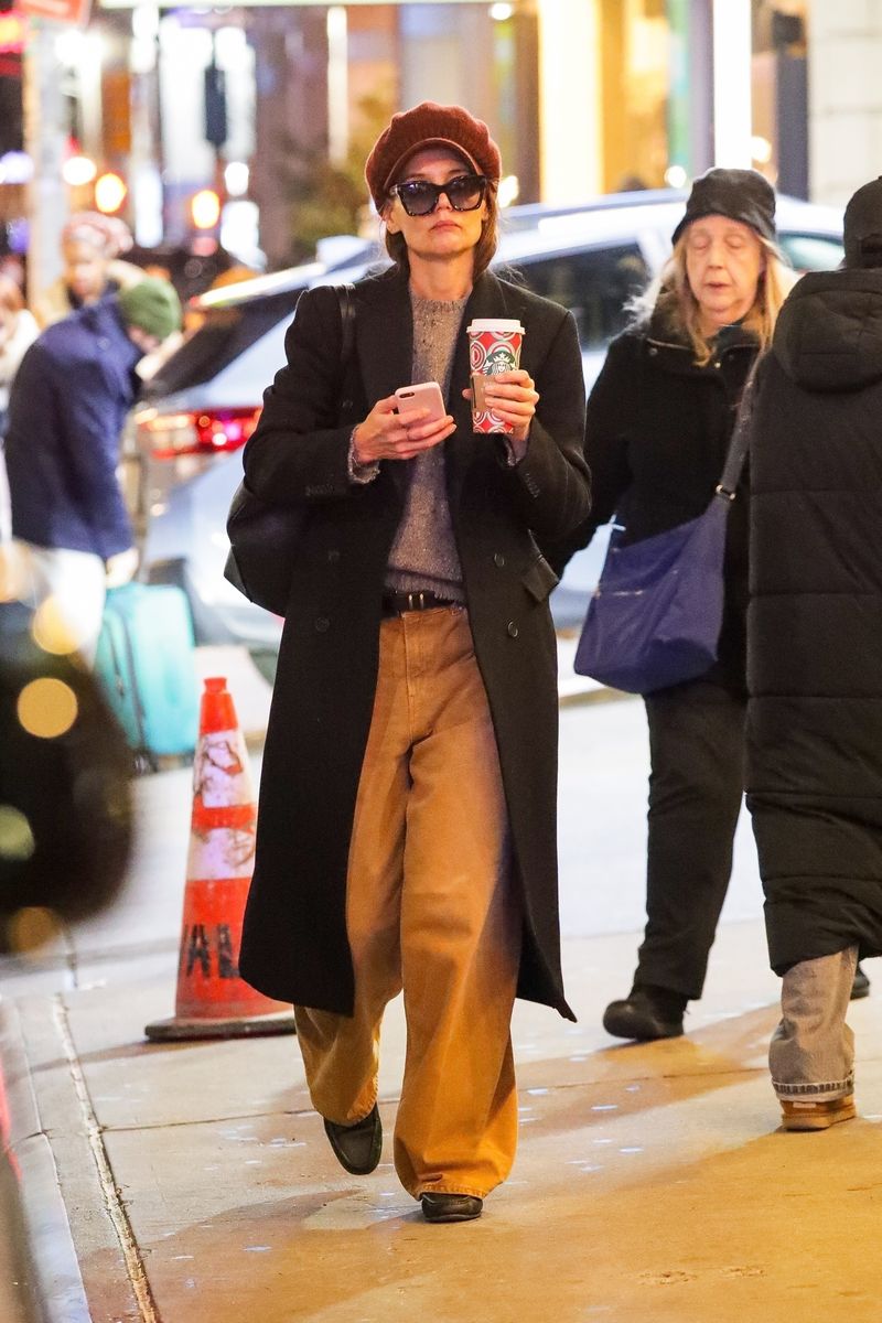 Katie Holmes lleva una gorra burdeos de vendedor de periódicos cuando llega al espectáculo de Broadway. "NUESTRO PUEBLO" en la ciudad de Nueva York. Katie luce elegante con pantalones holgados de color caqui y un abrigo largo negro.