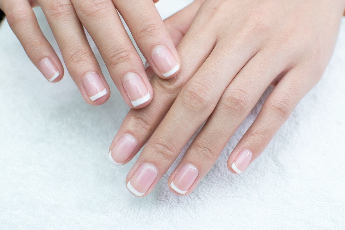 Close-up of hands with a classic French manicure featuring short nails with a natural pink base and crisp white tips, resting on a white towel.