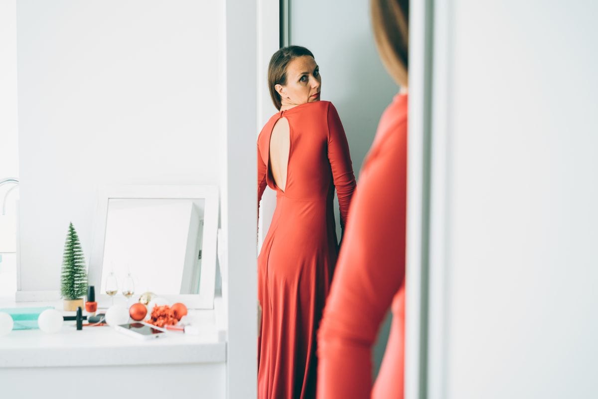 A woman getting dressed in a red dress.