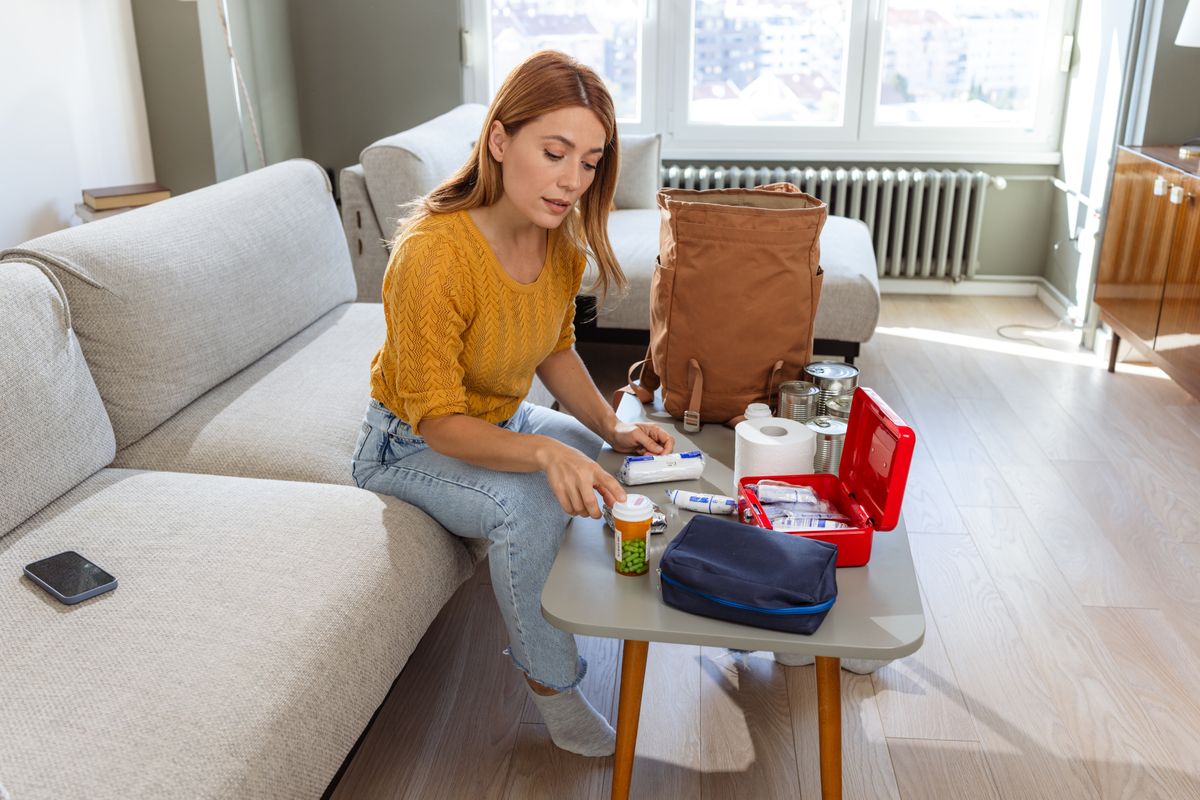 A woman carefully selects items like medication, first aid, and canned food as part of her survival kit for potential emergencies.