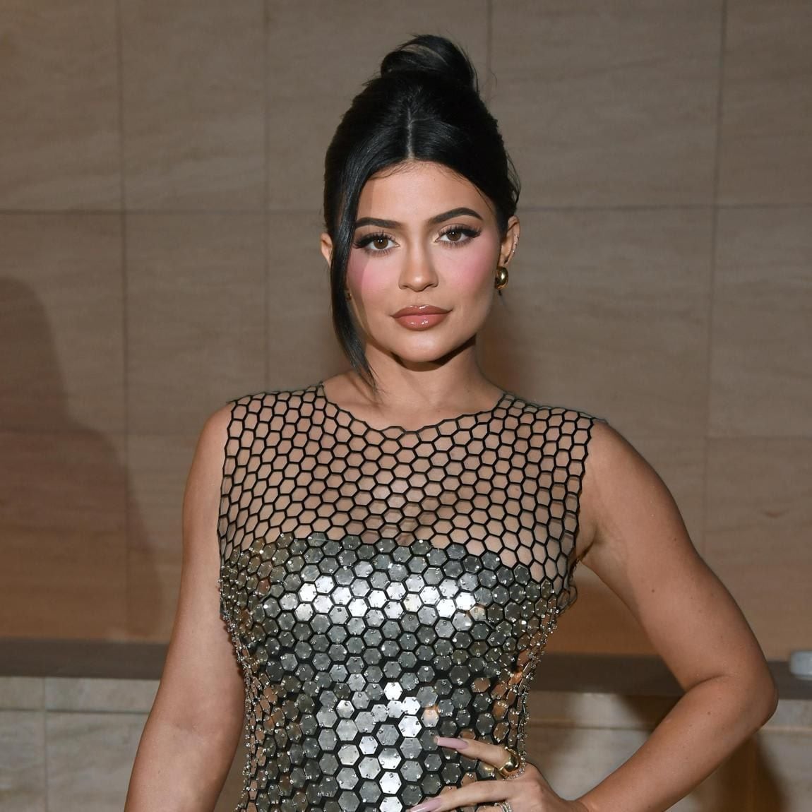 Kylie Jenner wearing an up-do with a loose strand on one side, rocking a silver dress with black details