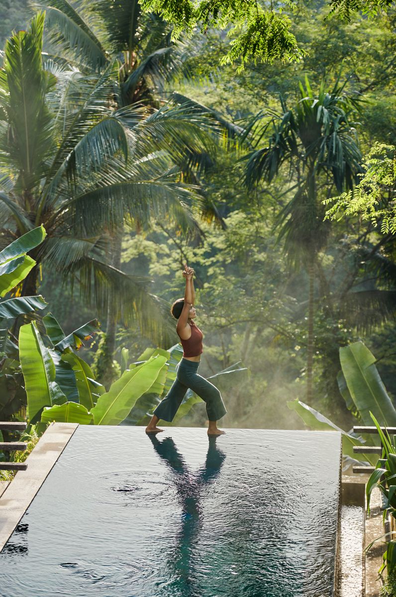 Asian woman practicing yoga next to infinity pool of luxury villa in Ubud, one of the world's most popular yoga centers