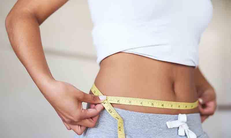 Woman measuring her toned abdomen with a tape measure