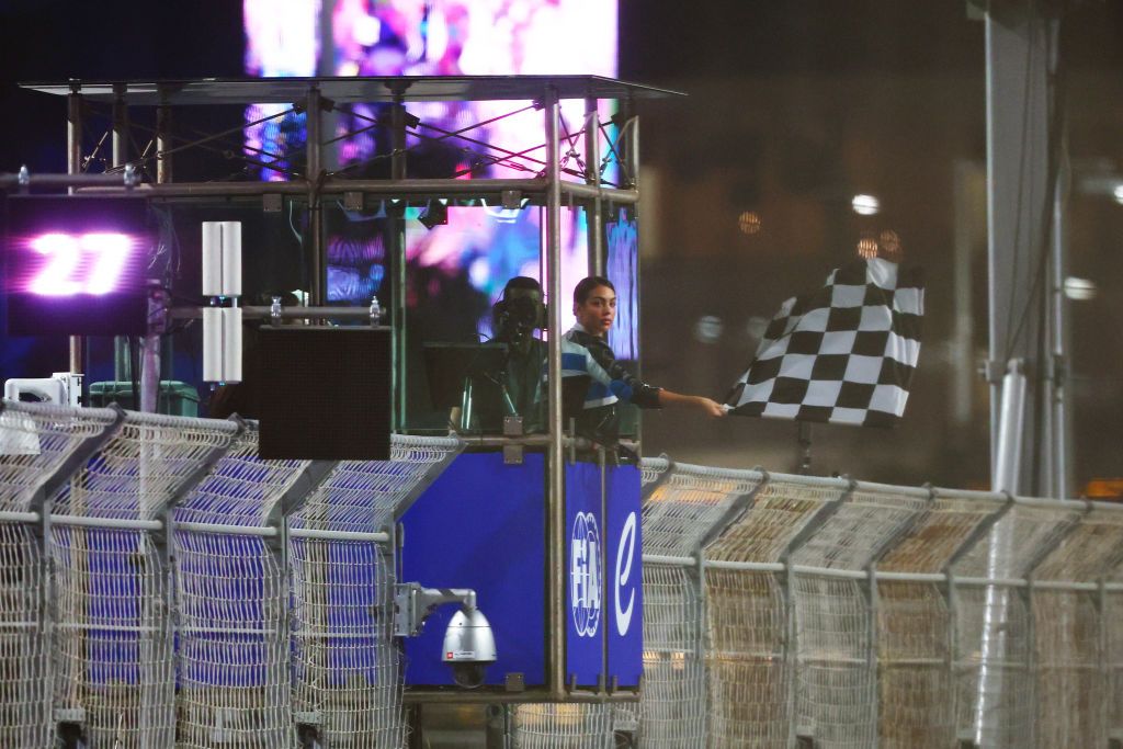 Georgina Rodríguez waving the checkered flag at Formula E Saudi Arabia from the race control tower at night.