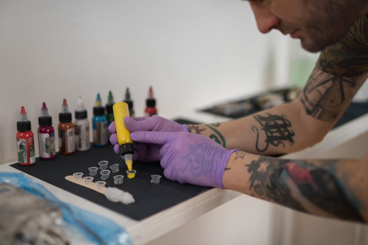 Male tattoo artist preparing for work and filling ink cup with color.