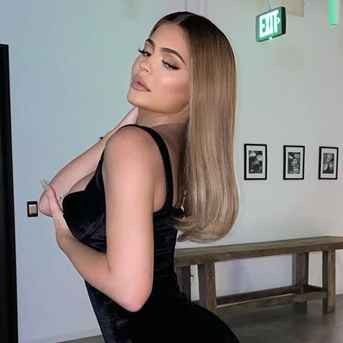 Kylie Jenner poses in a black dress with long honey blonde hair