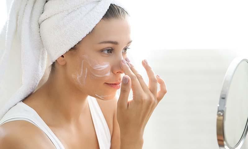 Young woman applies cream to her face