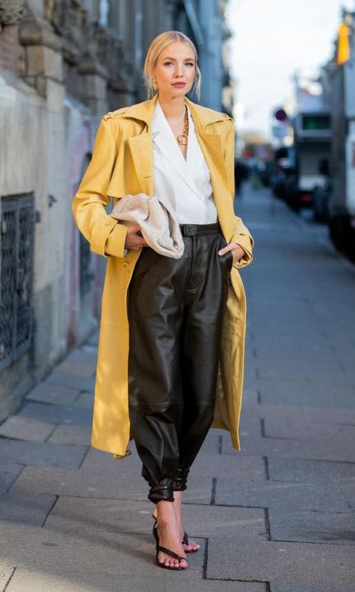 Leonie Hanne in a yellow coat, white blouse and ankle strap sandals done up over the bottom of her black leather pants