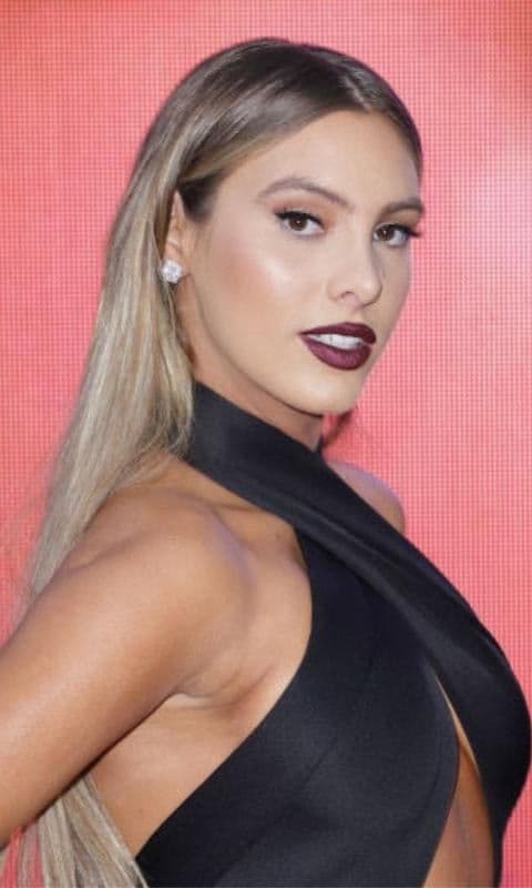 Lele Pons de perfil con cabello suelto y liso, con cutis radiante y uniforme