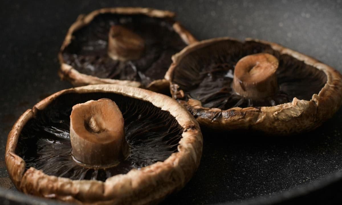 3 portobello mushrooms are being seared in a pan.