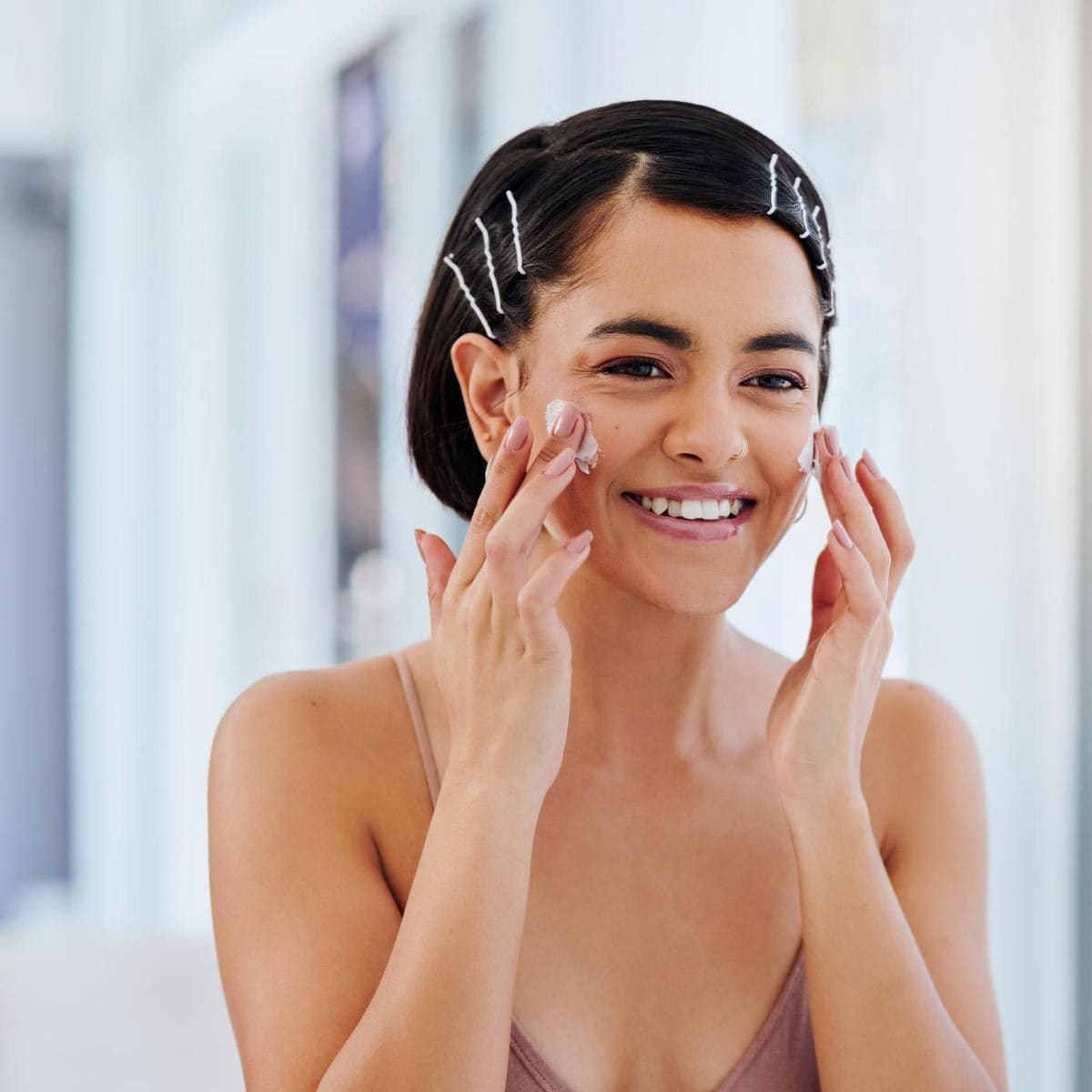 Shot of an attractive young woman applying moisturiser in front of a bathroom mirror