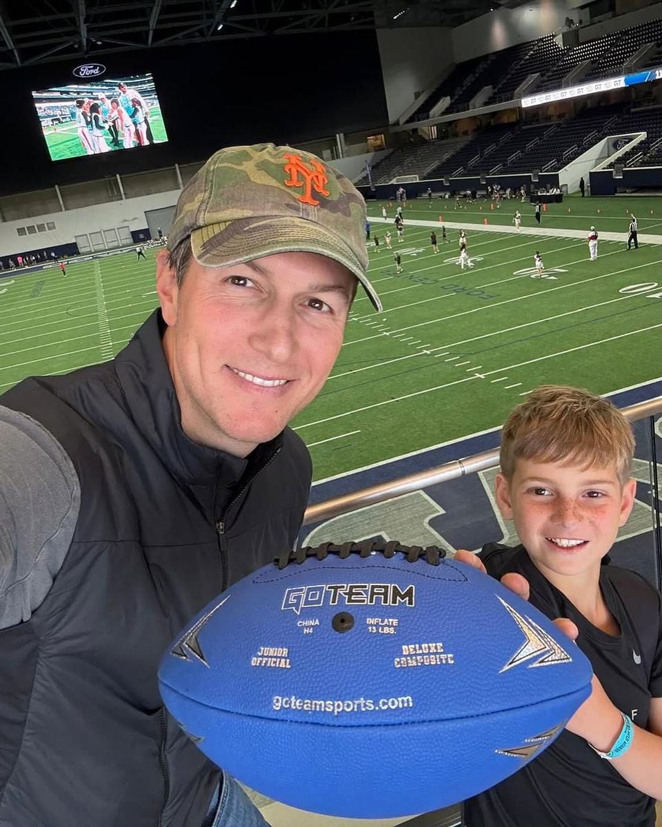 Jared and Theo smile while holding a blue football in a large inner stadium. 