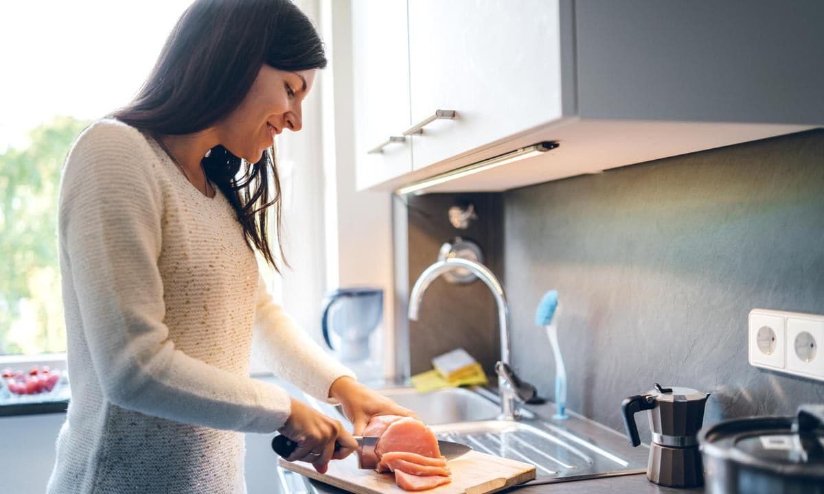 Young woman is cutting chicken meat on a wooden cutting board