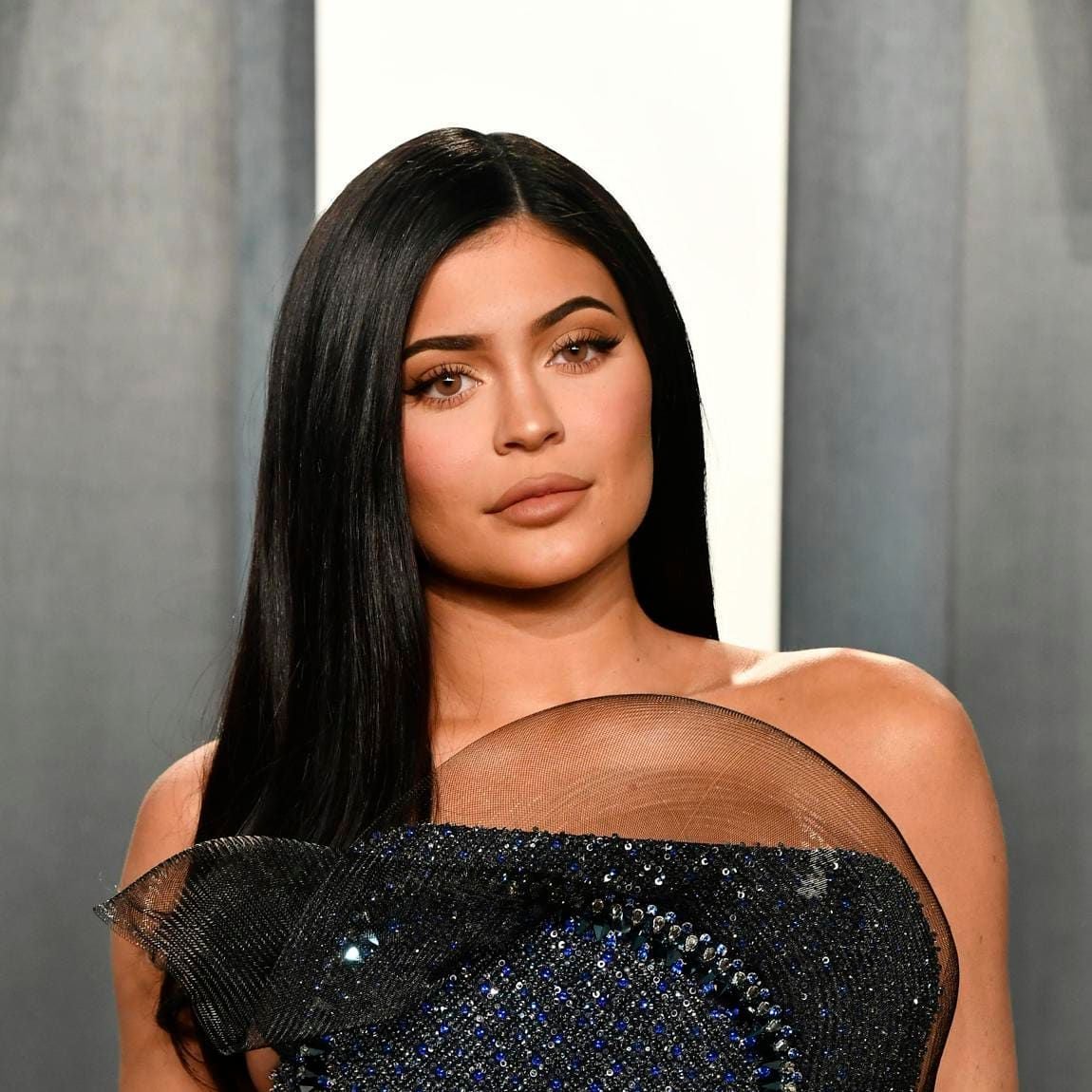 Kylie Jenner poses with straight dark hair in a shiny blue-black dress