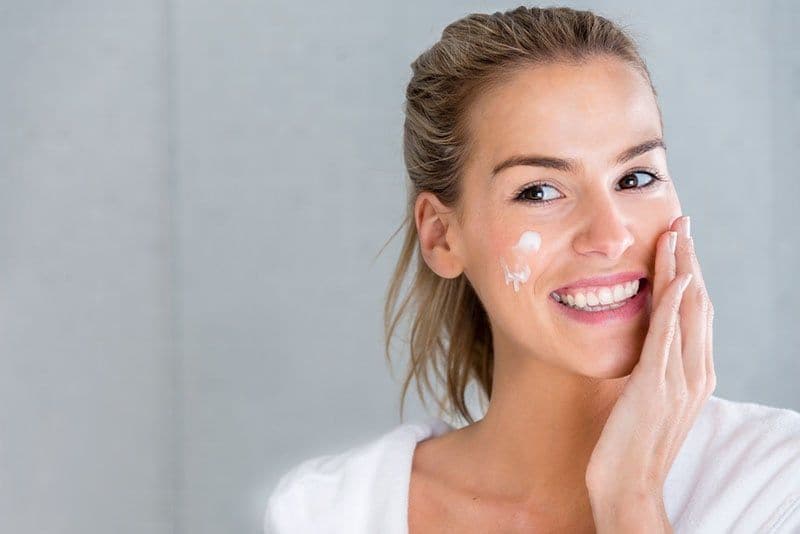 Young woman applies moisturizer cream to her face