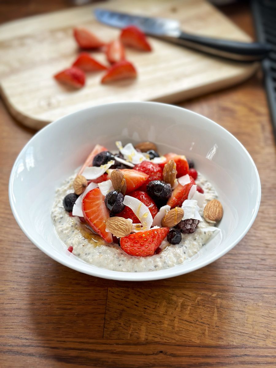 Bowl of overnight oats with fresh strawberry, , frozen blueberries, redcurrants, blackcurrants, raspberries and blackberries.