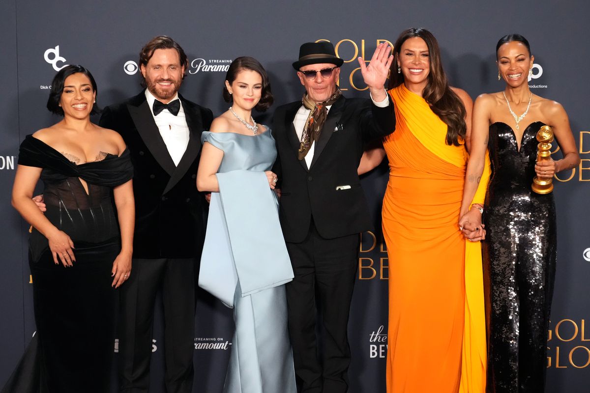 The full cast of Emilia Pérez, including Karla Sofía Gascón, Selena Gomez, Zoe Saldaña, and Adriana Paz, posing with director Jacques Audiard at a formal event.