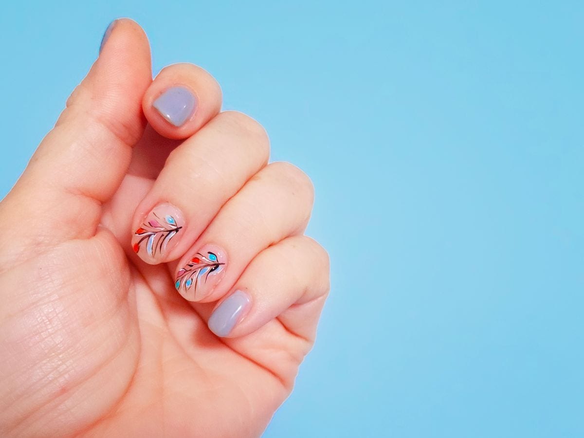 Delicate beauty of a hand adorned with a pale gray - blue manicure featuring a leafy plant design