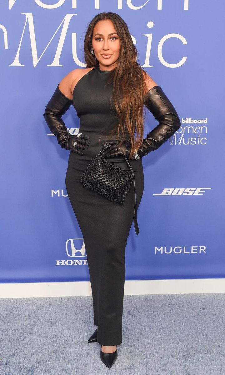 Adrienne Bailon wearing all black with latex gloves and a matching purse.